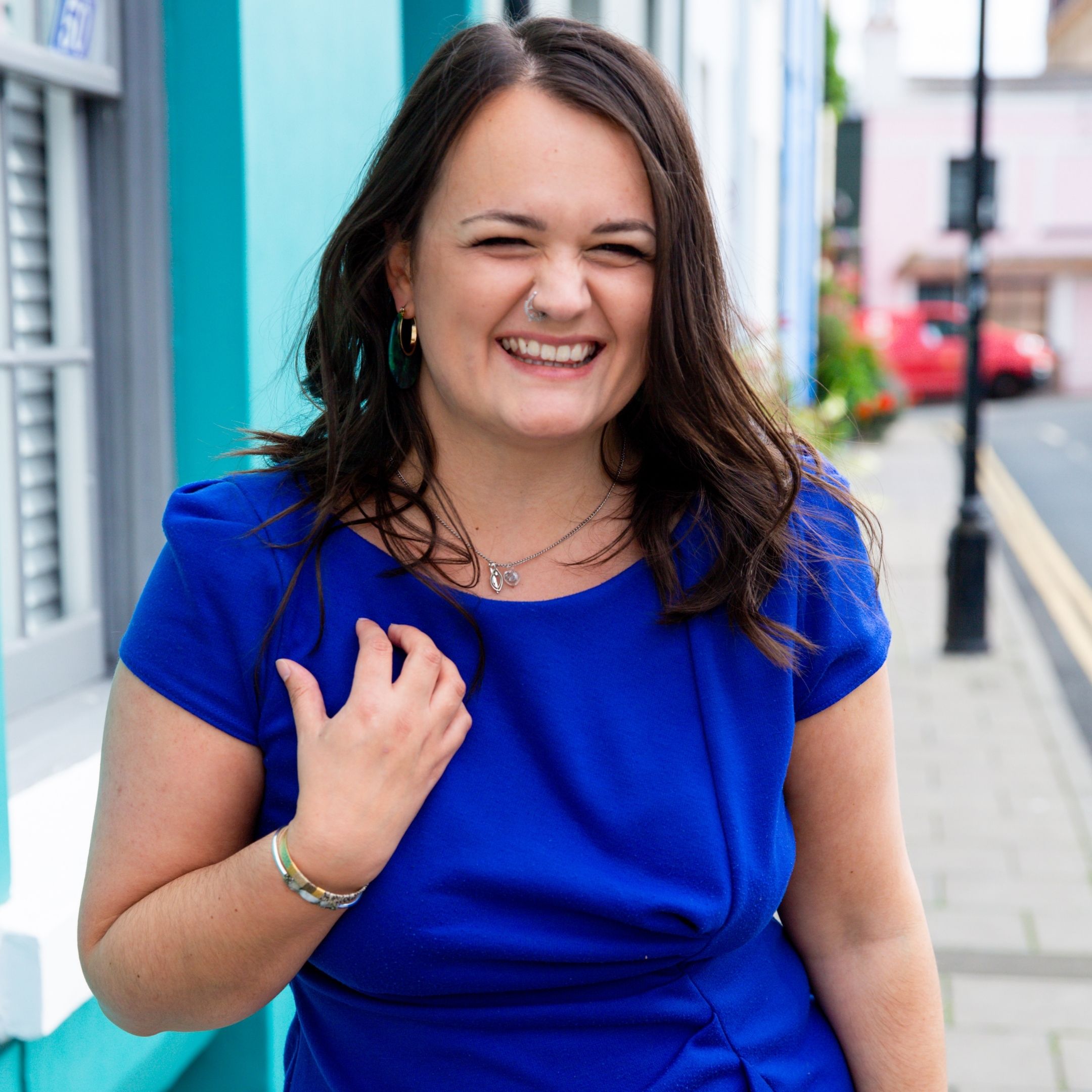 Lucy smiles wearing a royal blue dress in front of a bright blue house in Brighton